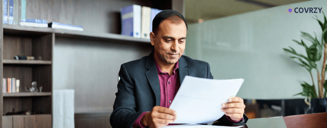 An Indian middle-ages man wearing a dark suit reading document in a corporate chamber
