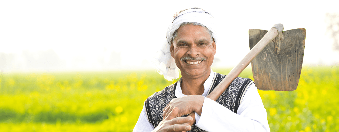 A farmer smiling holding a ploughing axe under the Pradhan Mantri Fasal Bima Yojana scheme