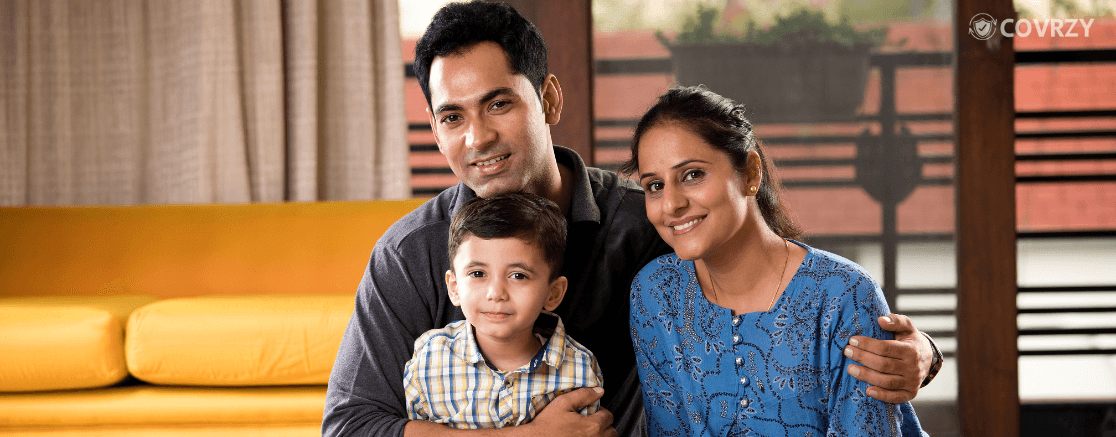 An Indian father with his wife and his child, smiling while looking at the camera, behind is a yellow sofa