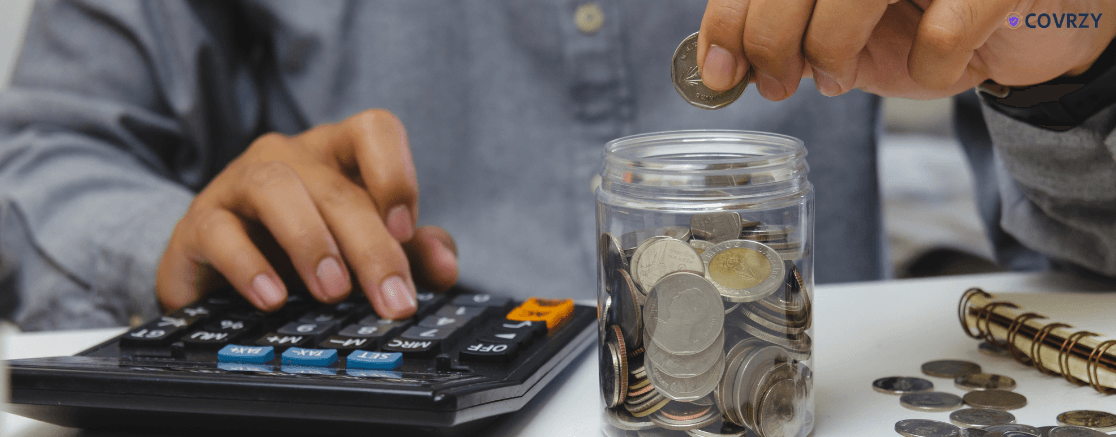 an individual's hand putting some coins in a jar with a calculator beside him